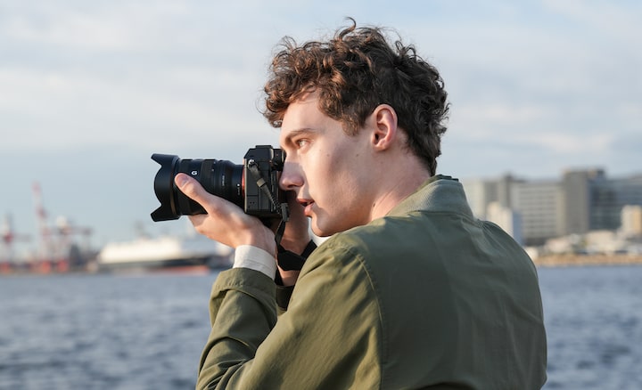 Man shooting in coastal location with camera hand-held, using viewfinder