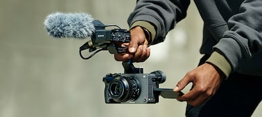 Usage image of a videographer holding the FX2 equipped with an XLR handle and microphone while filming a video