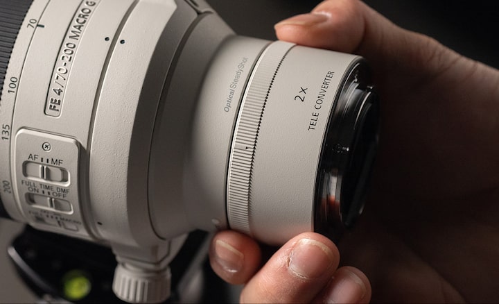 Usage image showing user holding lens with 2.0&times; teleconverter mounted