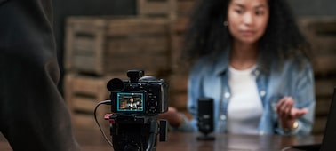 Usage image of a videographer operating the FX2 mounted on a tripod, live streaming a woman speaking into a microphone