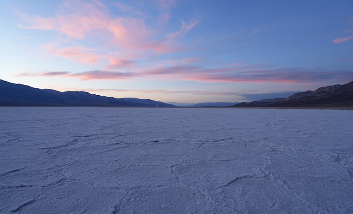 Wide-angle shot of desert landscape with sunset behind distant mountains