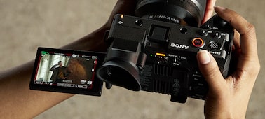 Usage image of a videoprapher holding the FX2 with the LCD monitor angled outwards, filming a video