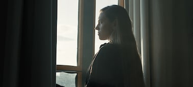 Example image of a woman looking at scenery outside a window, her form silhouetted between two curtains