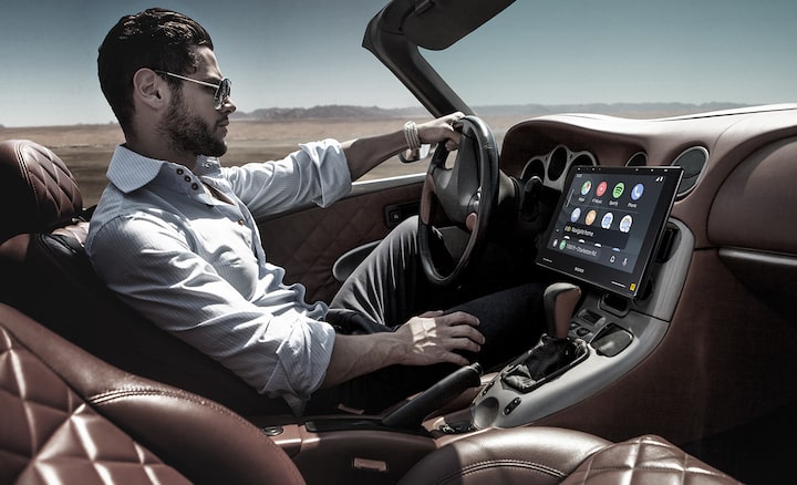 The 10.1" (25.7cm) Mobile ES™ High-Resolution Digital Media Receiver seen in-situ on a car dashboard as a man drives the car along a desert road.
