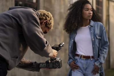 Usage image of a man bent over holding an FX2 by an XLR handle, filming a woman walking