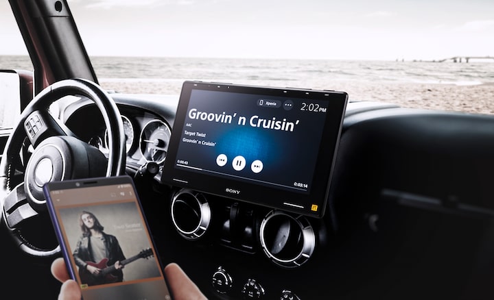The 10.1" (25.7cm) Mobile ES™ High-Resolution Digital Media Receiver seen in-situ on a car dashboard, with a phone in the foreground indicating the connectivity.