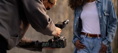 Usage image of a man bent over holding an FX2 by an XLR handle, filming a woman walking