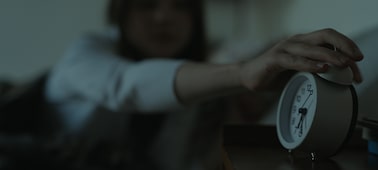 Example image of an alarm clock in focus in the foreground, with a woman reaching to stop the alarm in the bokeh background