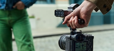 Usage image of a videographer holding the FX2 by an XLR handle in his right hand, filming a subject