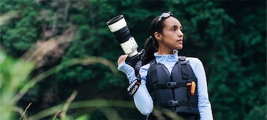 Woman carrying a camera with a super-telephoto lens on her shoulder outdoors
