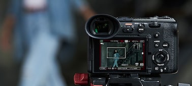Usage image of the FX2 mounted on a tripod in focus in the foreground, using the Auto Framing feature to track a woman walking in the bokeh background